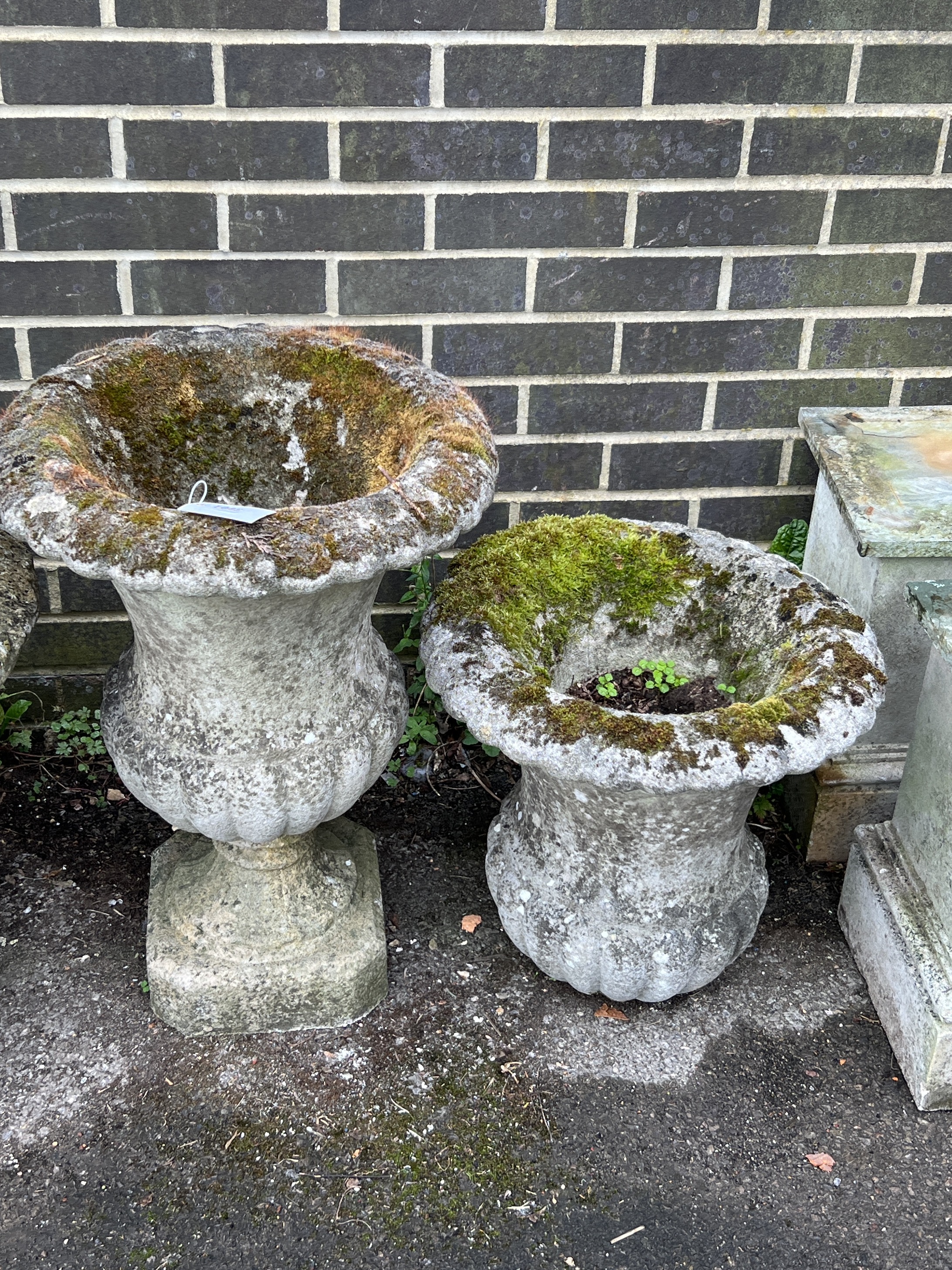 A pair of reconstituted stone circular campana garden urns, one lacks base, larger diameter 44cm, height 64cm